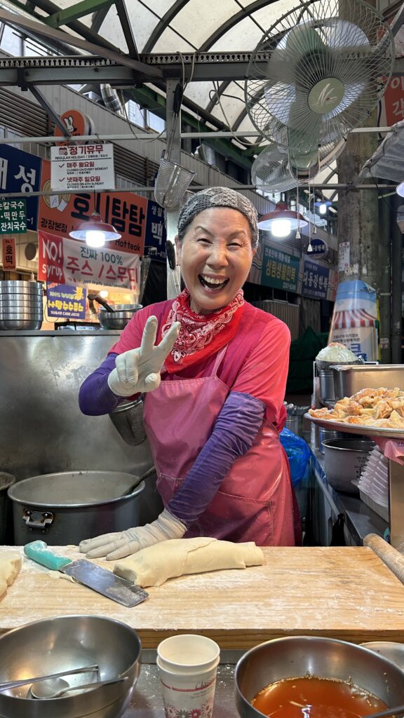 Korean lady making noodles, smiling and doing the peace sign