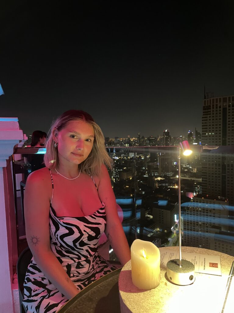 A girl sat on a rooftop bar at night with the city skyline behind her